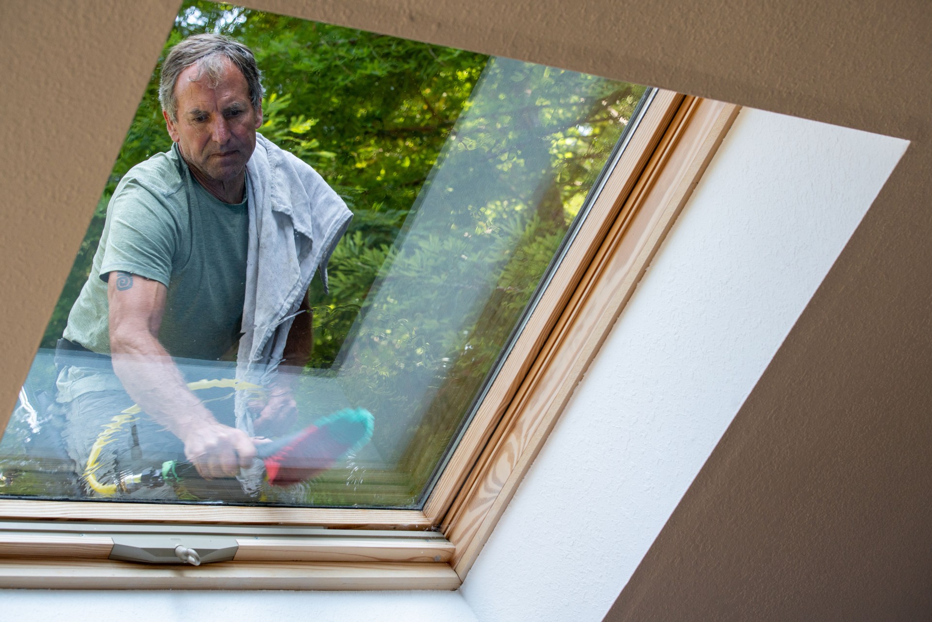 Man washing skylight on roof of house
